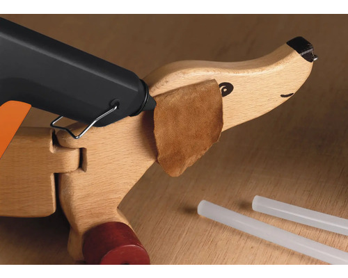 Heissklebepistole beim Anbringen eines Stoffstücks an einen Holzspielzeughund mit Klebesticks