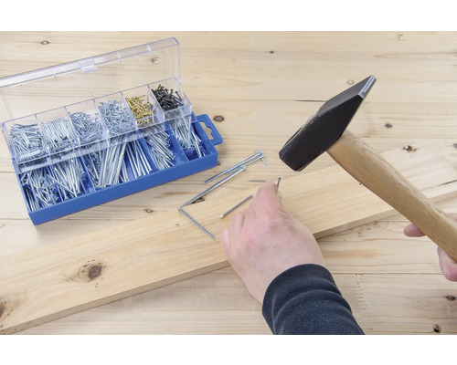 Marteau enfonçant un clou dans une planche de bois à côté d''une boîte d''assortiment de clous.