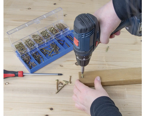 Visseuse sans fil en train de visser une vis dans une pièce de bois, assortiment de vis et tournevis en arrière-plan