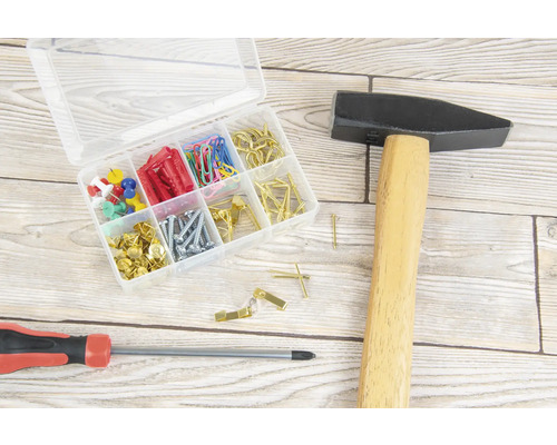 Hammer, Schraubenzieher und Sortimentskasten mit Schrauben, Dübeln, Nägeln, Reißzwecken und Büroklammern auf einer Holzoberfläche