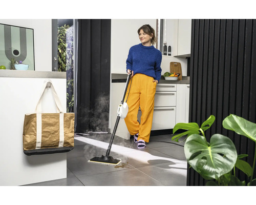 Une femme utilise un nettoyeur à vapeur dans une cuisine avec un sac de courses accroché au mur