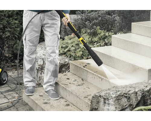 Une personne nettoie un escalier en pierre avec un nettoyeur haute pression.