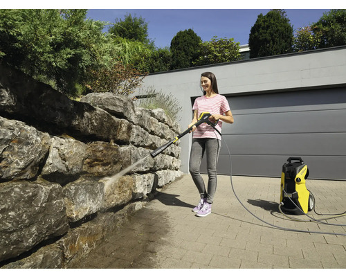 Une femme nettoie un mur en pierre avec un nettoyeur haute pression à l''extérieur.