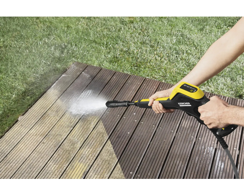 Une personne nettoie une terrasse en bois avec un nettoyeur haute pression