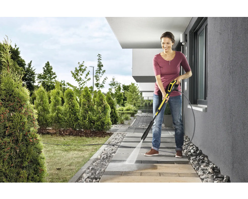Une femme nettoie des pavés devant la maison avec un nettoyeur haute pression