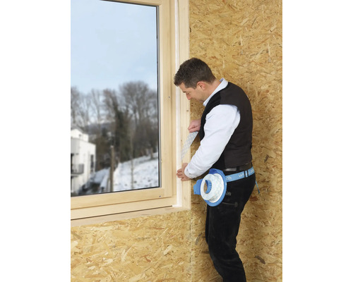 Handwerker montiert Dichtband an einem Fensterrahmen aus Holz.