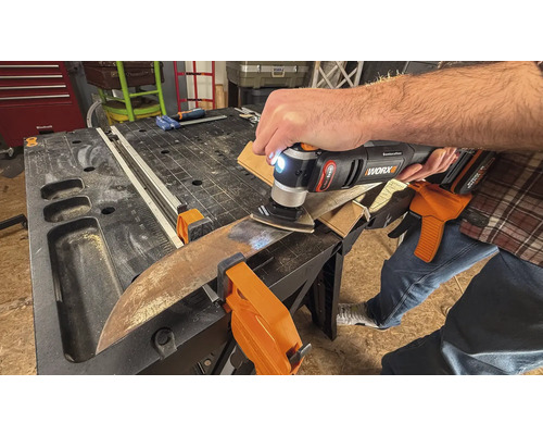 Eine Person verwendet ein Multifunktionswerkzeug zum Schleifen eines Werkstücks, das mit Klemmen auf einer Werkbank befestigt ist.