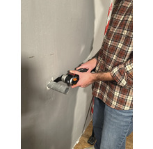 Mann schneidet Rohr mit einem Multifunktionswerkzeug an einer Wand.