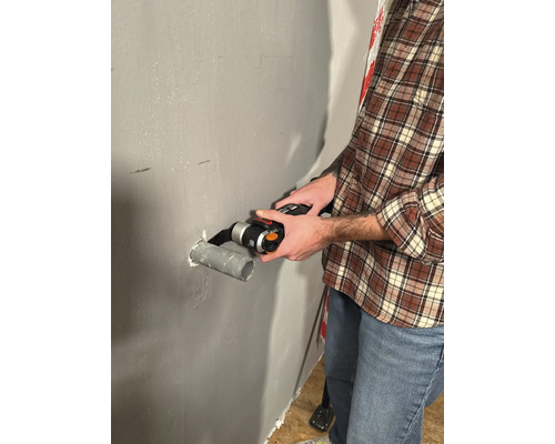 Mann schneidet Rohr mit einem Multifunktionswerkzeug an einer Wand.