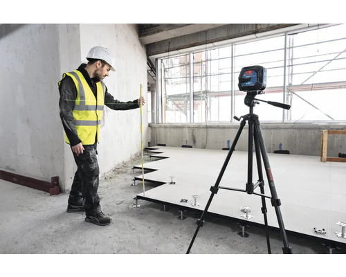 Artisan avec niveau laser et latte de nivellement lors de l''installation d''un plancher surélevé.
