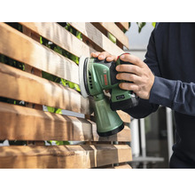 Eine Person schleift mit einem Akku-Exzenterschleifer einen Holzzaun.