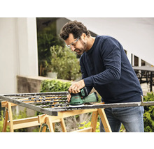 Mann schleift Metallgitter mit einem Exzenterschleifer im Freien