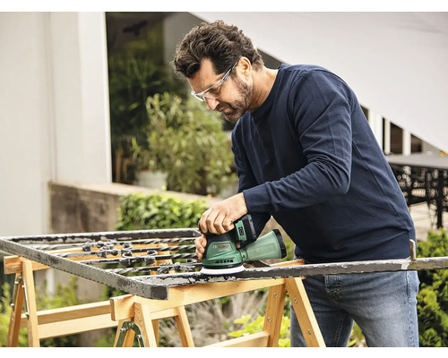 Mann schleift Metallgitter mit einem Exzenterschleifer im Freien