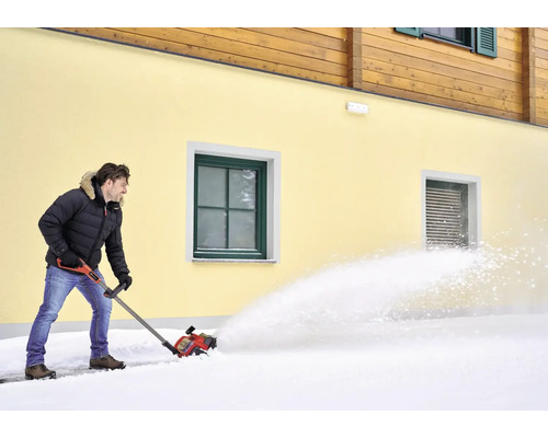 Un homme déblaie la neige avec une fraise à neige devant une maison
