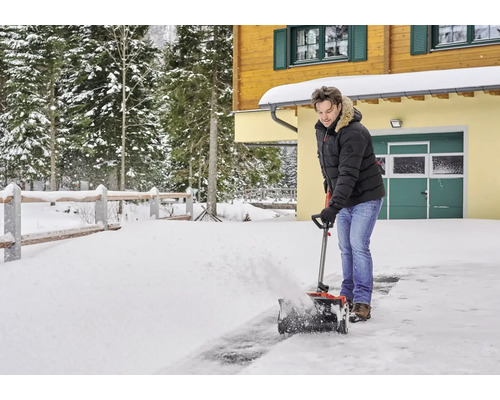 Un homme déblaie la neige devant une maison avec une souffleuse à neige