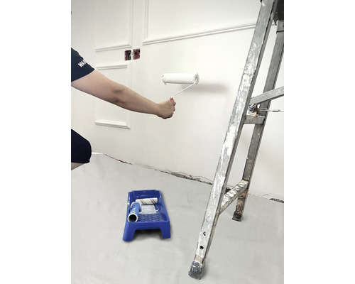 Une personne peint un mur avec un rouleau à peinture, un bac à peinture et une échelle dans la pièce.