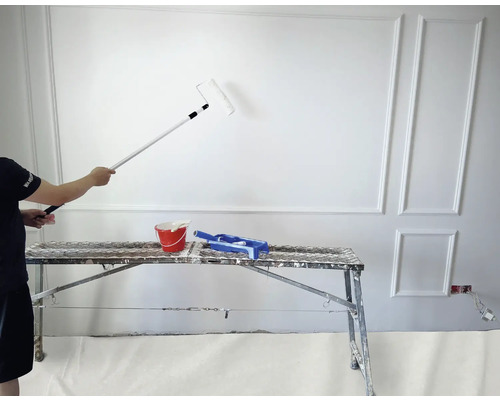 Une personne peint un mur avec un rouleau à peinture, à l''aide d''une échelle, d''un pot de peinture et d''un bac à peinture.