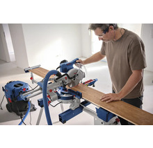 Mann arbeitet mit einer Bosch Kappsäge an einem Holzbrett, mit Staubsauger und Gehörschutz