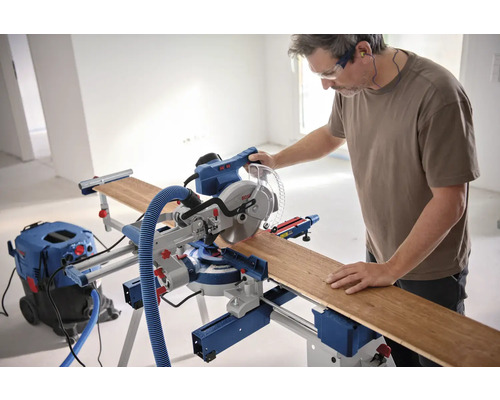 Mann arbeitet mit einer Bosch Kappsäge an einem Holzbrett, mit Staubsauger und Gehörschutz