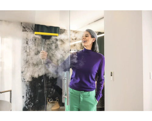 Femme nettoie paroi de verre avec un nettoyeur à vapeur dans une salle de bains