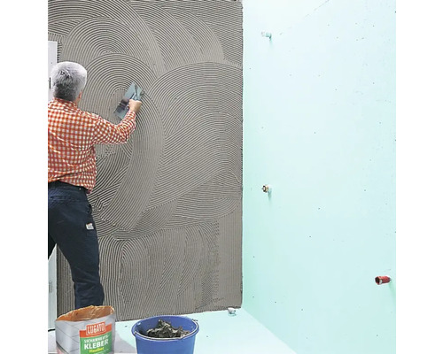 Un artisan applique de la colle à carrelage sur un mur de salle de bains.