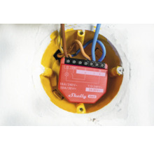 Gros plan d''un relais Shelly Gen3 dans un boîtier encastré jaune avec des câbles électriques.