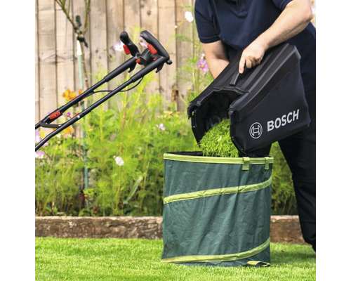 Une personne vide l''herbe coupée d''un bac de ramassage de tondeuse à gazon dans un sac de jardin. Une tondeuse à gazon est visible en arrière-plan. Logo Bosch.