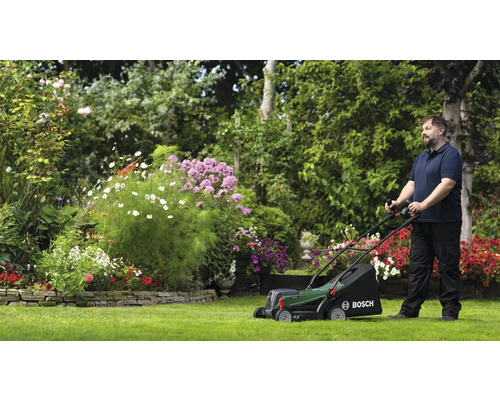 Homme tondant le gazon avec une tondeuse à gazon Bosch dans un jardin fleuri