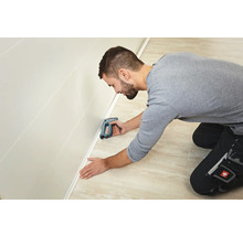 Handwerker befestigt eine Sockelleiste mit einem Tacker an einer Wand.