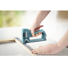Une personne utilise une agrafeuse manuelle Novus pour fixer une toile sur un cadre en bois.