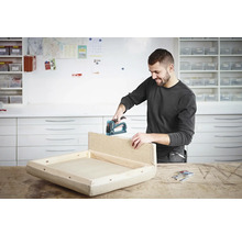 Un homme fixe une pièce de bois avec une agrafeuse sur un cadre dans un atelier
