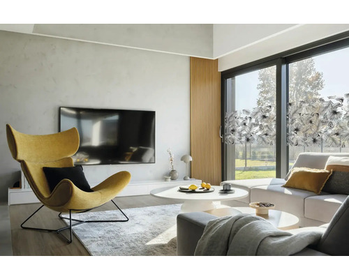 Heller Wohnraum mit Sessel, Couch und Fensterfolie mit Pflanzenmuster.