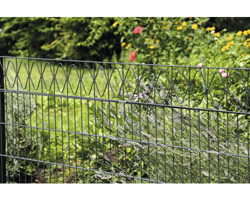 Clôture de jardin avec partie supérieure décorative devant des plantes vertes