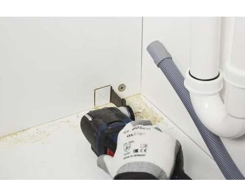 Une personne utilise un outil multifonction pour découper une armoire près d''un drain.
