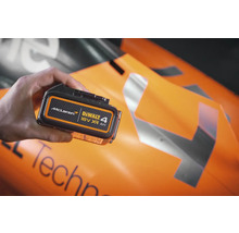 Dewalt 18-Volt-XR-4-Ah-Akkupack in der Hand vor einem McLaren Formel-1-Wagen.