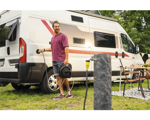 Mann schliesst Wohnmobil an Stromkabeltrommel auf Campingplatz an