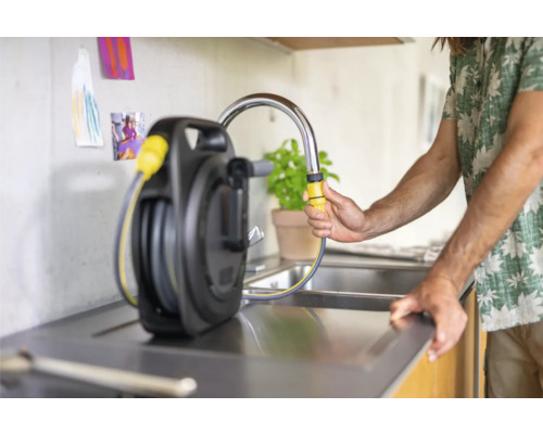 Aufgerollter Gartenschlauch mit Schlauchanschluss am Wasserhahn in der Küche.