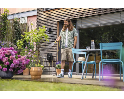 Mann bewässert Pflanzen mit einer Schlauchtrommel im Garten.