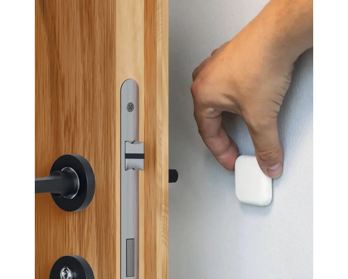 Une main fixe un butoir de porte magnétique sur un mur à côté d''une porte en bois avec une serrure de porte argentée.