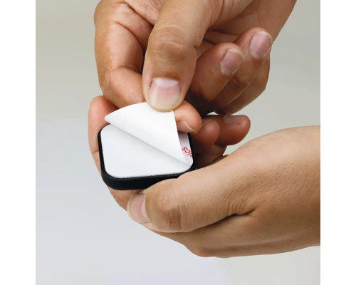 Une main retire le film protecteur d''un patin de meuble autocollant.