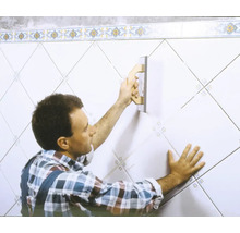 Un homme joint des carreaux sur un mur avec une taloche à joints.