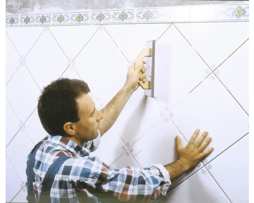Un homme joint des carreaux sur un mur avec une taloche à joints.