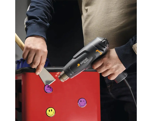 Un artisan retire des autocollants d''une boîte à outils avec un décapeur thermique.