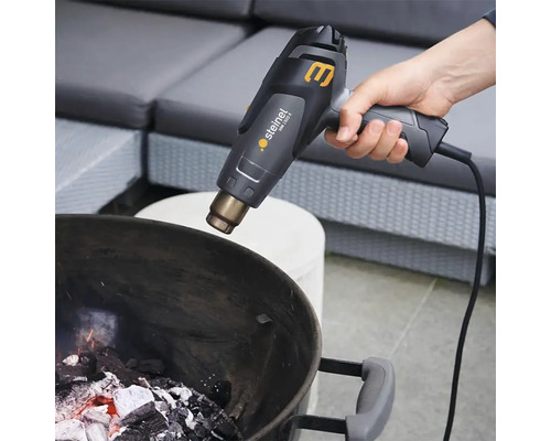 Eine Hand hält ein Heissluftgebläse über einem Grill mit glühenden Kohlen.