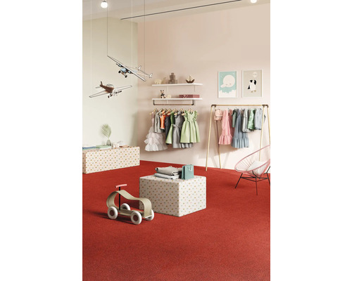 Magasin de vêtements pour enfants avec des robes, des avions jouets et des jouets en bois sur un tapis rouge.