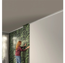 Femme tapissant un mur avec du papier peint à motifs de feuilles