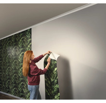 Femme fixant du papier peint à feuilles vertes sur le mur