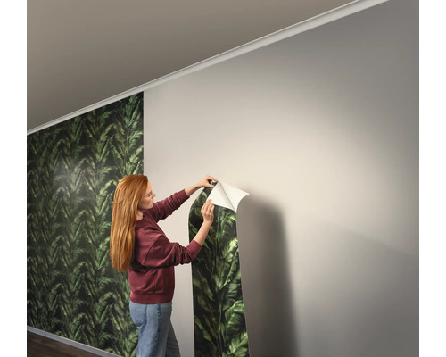 Femme fixant du papier peint à feuilles vertes sur le mur