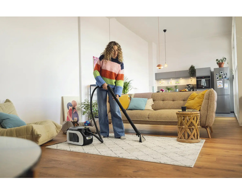 Une femme nettoie un tapis avec un aspirateur-laveur dans un salon.