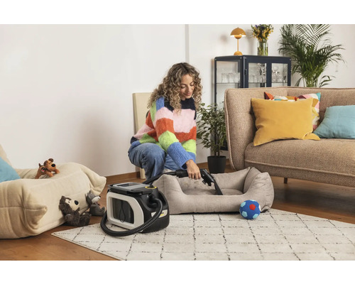 Une femme nettoie un lit pour animaux avec un aspirateur laveur dans un salon.